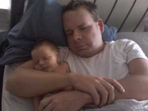 A father lays in bed with his two-day old son, both resting with their profiles side-by-side.